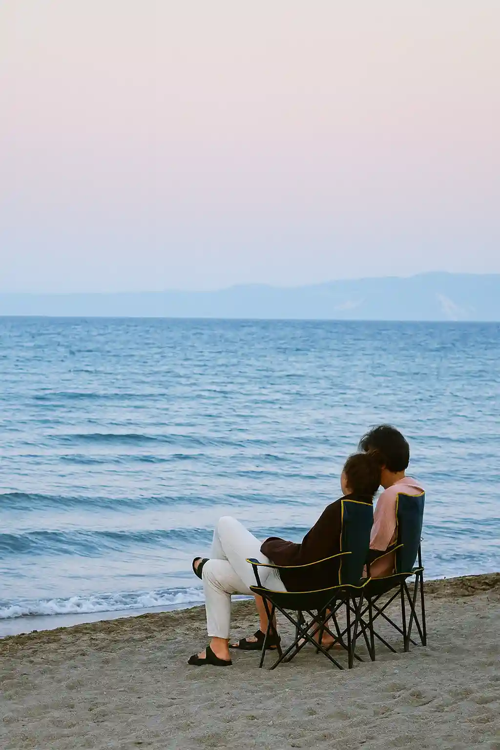Pareja sentada frente al mar disfrutando de un momento tranquilo al atardecer, ideal para ilustrar la sección sobre nosotros.